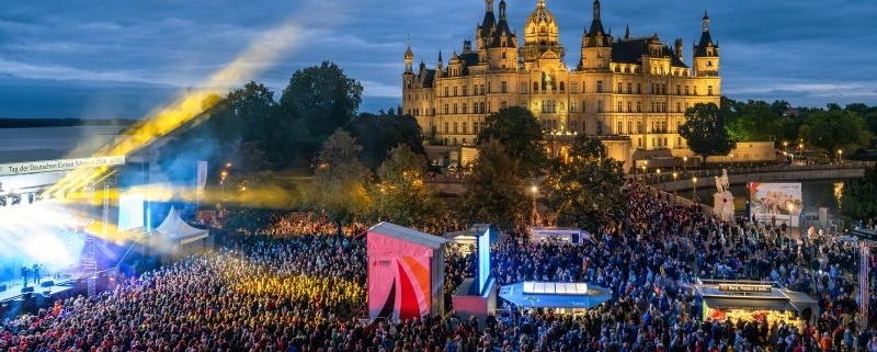 Das Bild zeigt Besuchende beim Konzert von Roland Kaiser sowie das Schweriner Schloss am Abend