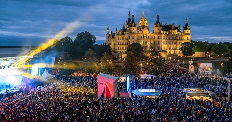 Das Bild zeigt Besuchende beim Konzert von Roland Kaiser sowie das Schweriner Schloss am Abend