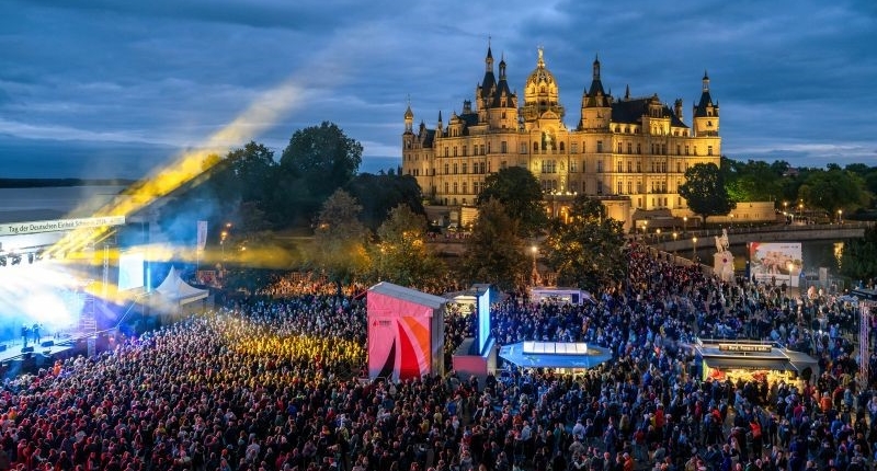 Das Bild zeigt Besuchende beim Konzert von Roland Kaiser sowie das Schweriner Schloss am Abend