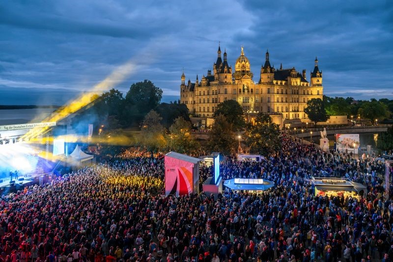 Das Bild zeigt Besuchende beim Konzert von Roland Kaiser sowie das Schweriner Schloss am Abend