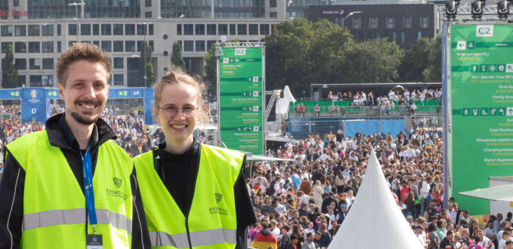 Das Bild zeigt einen Sicherheitsmager und eine Sicherheitsmanagerin der FAN ZONE in Hamburg. Im Hintergrund sieht man Fans im Bereich des Public Viewings