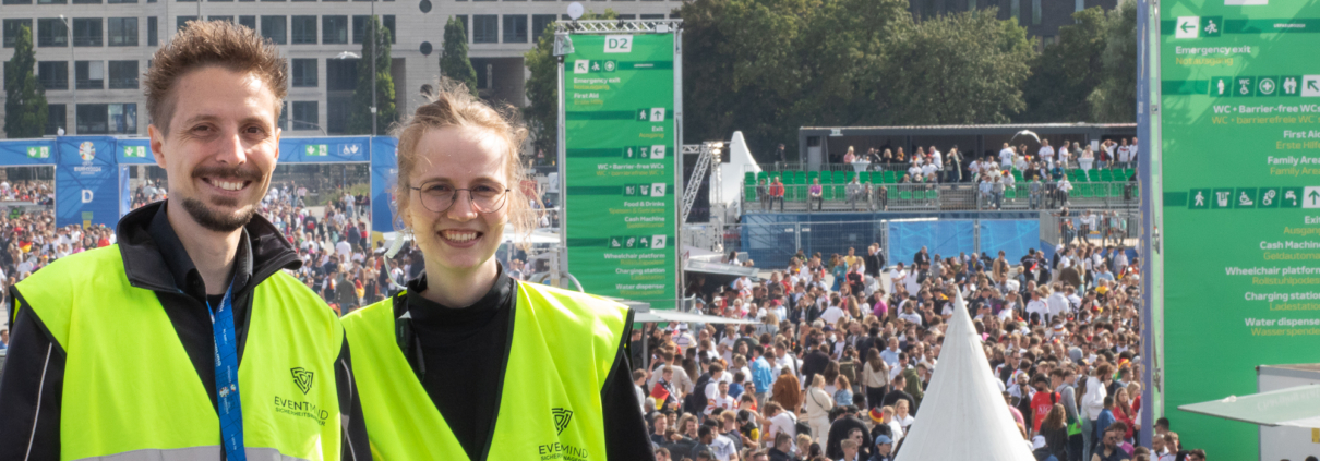 Das Bild zeigt einen Sicherheitsmager und eine Sicherheitsmanagerin der FAN ZONE in Hamburg. Im Hintergrund sieht man Fans im Bereich des Public Viewings