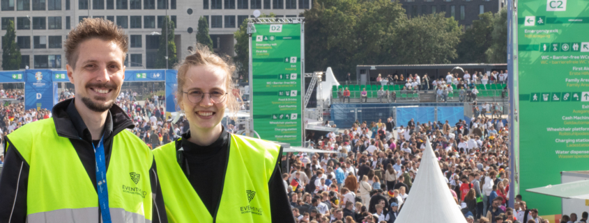 Das Bild zeigt einen Sicherheitsmager und eine Sicherheitsmanagerin der FAN ZONE in Hamburg. Im Hintergrund sieht man Fans im Bereich des Public Viewings